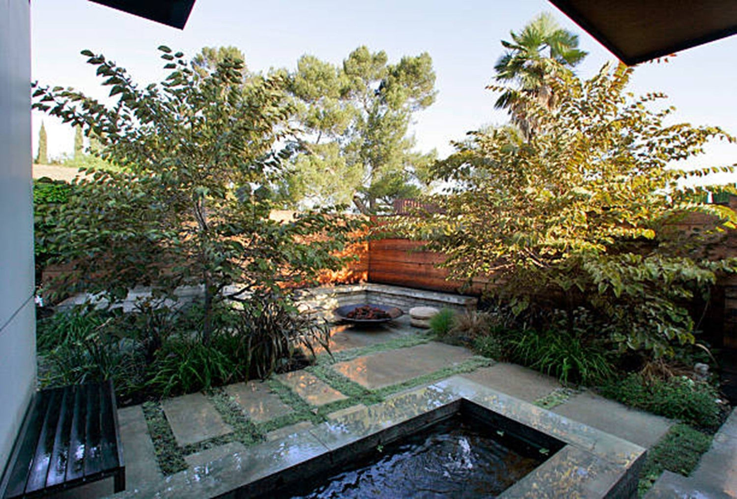 A backyard patio featuring a small cold plunge pool with a fire pit surrounded by greenery and seating.